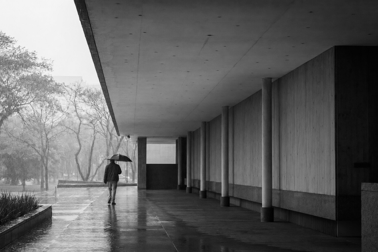 Pessoa com guarda-chuva sob uma marquise em dia de chuva